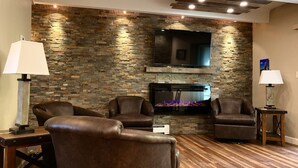 Uma sala de estar com parede de pedra, televisão de tela plana, lareira, poltronas de couro e piso de madeira.