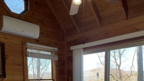 A wooden cabin bedroom with a large bed, a chair by the window, and a view of the outdoors.
