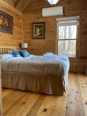 Quarto de cabana de madeira com cama, um quadro, janela e ar condicionado.
