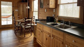 A wooden cabin interior with a dining area, kitchen, and a sign that reads "GATHER WITH A GRATEFUL HEART".