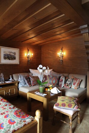A cozy room with a wooden ceiling, a sofa with patterned cushions, a small table with a vase of flowers, and wall-mounted lights. - Kristiania Lech (Lech am Arlberg)