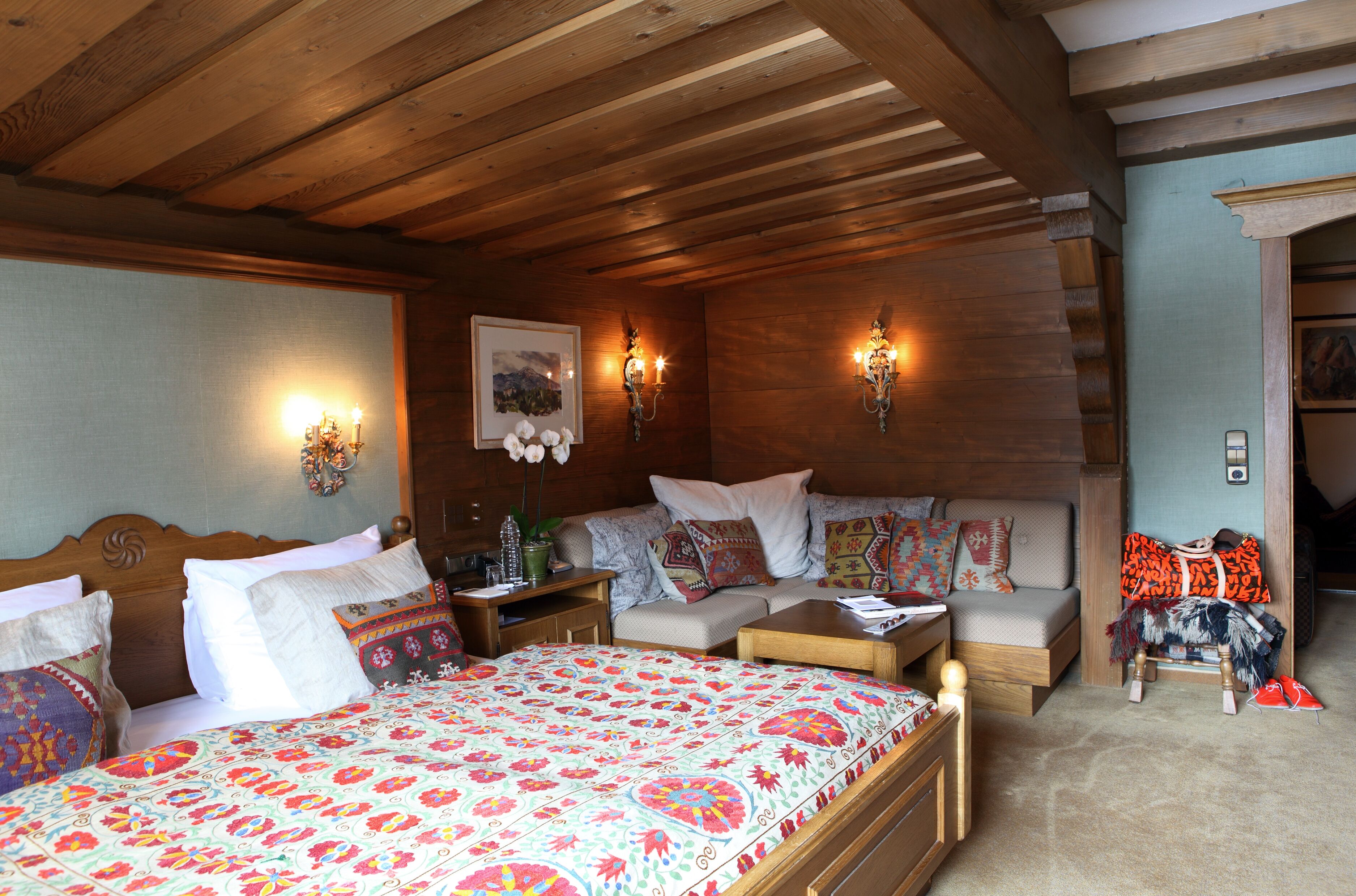 Una habitación acogedora con techo de madera, una cama con colcha estampada, un sofá con cojines decorados y una mesita con lámpara.