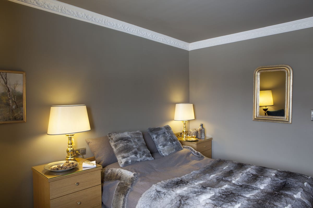 Une chambre à coucher avec un lit, deux tables de chevet avec des lampes, un miroir et un tableau encadré accroché au mur.