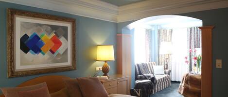A hotel room with a bed, a desk with a lamp, a chair, and a view of the outside.