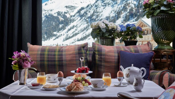 A breakfast table with a mountain view, a plaid sofa, and a vase of flowers.