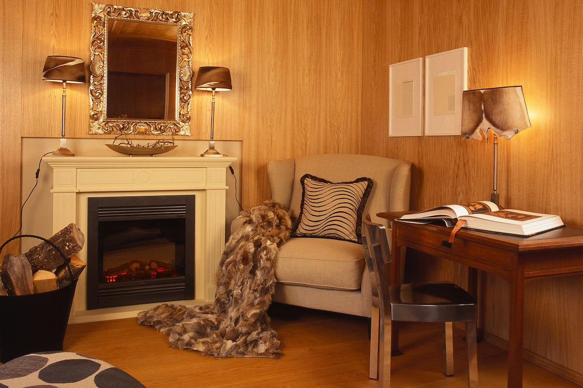 Un salon chaleureux avec une cheminée, un canapé, un fauteuil et une table sur laquelle repose un livre.
