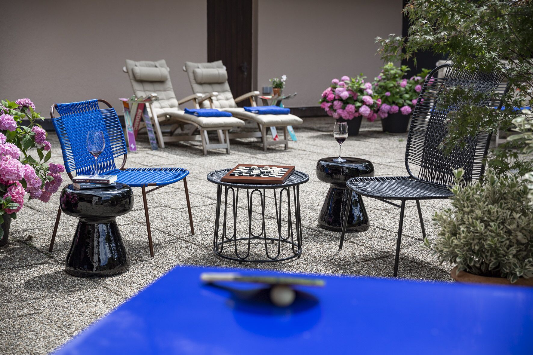 A patio area with lounge chairs, a chess table, and a small table with a glass of wine.
