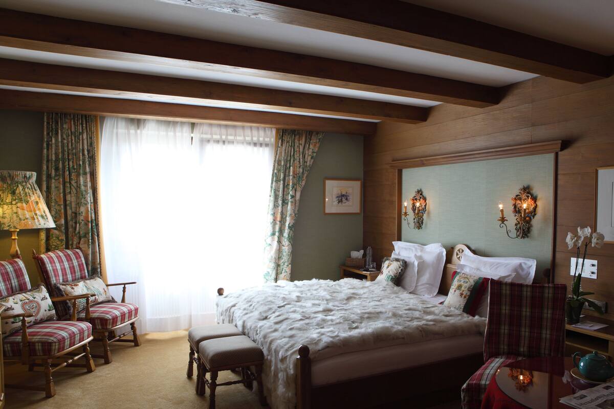Une chambre confortable avec un grand lit, deux fauteuils, une petite table avec une théière et une fenêtre avec des rideaux.