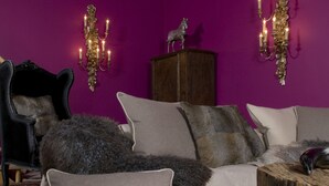 A room with a purple wall, a sofa with multiple cushions, a wooden side table, a chandelier, and a mounted deer head.