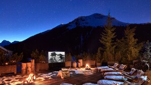 An outdoor cinema with a fire, lounge chairs, and a mountain backdrop.
