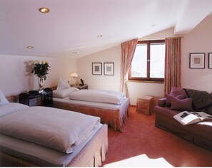 Relax in this inviting room with two single beds, a nightstand, and a comfortable armchair by the window.