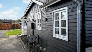 En boligbygning med grå facade, hvide vinduesrammer, en synlig garageport og en indkørsel der fører til en grussti.