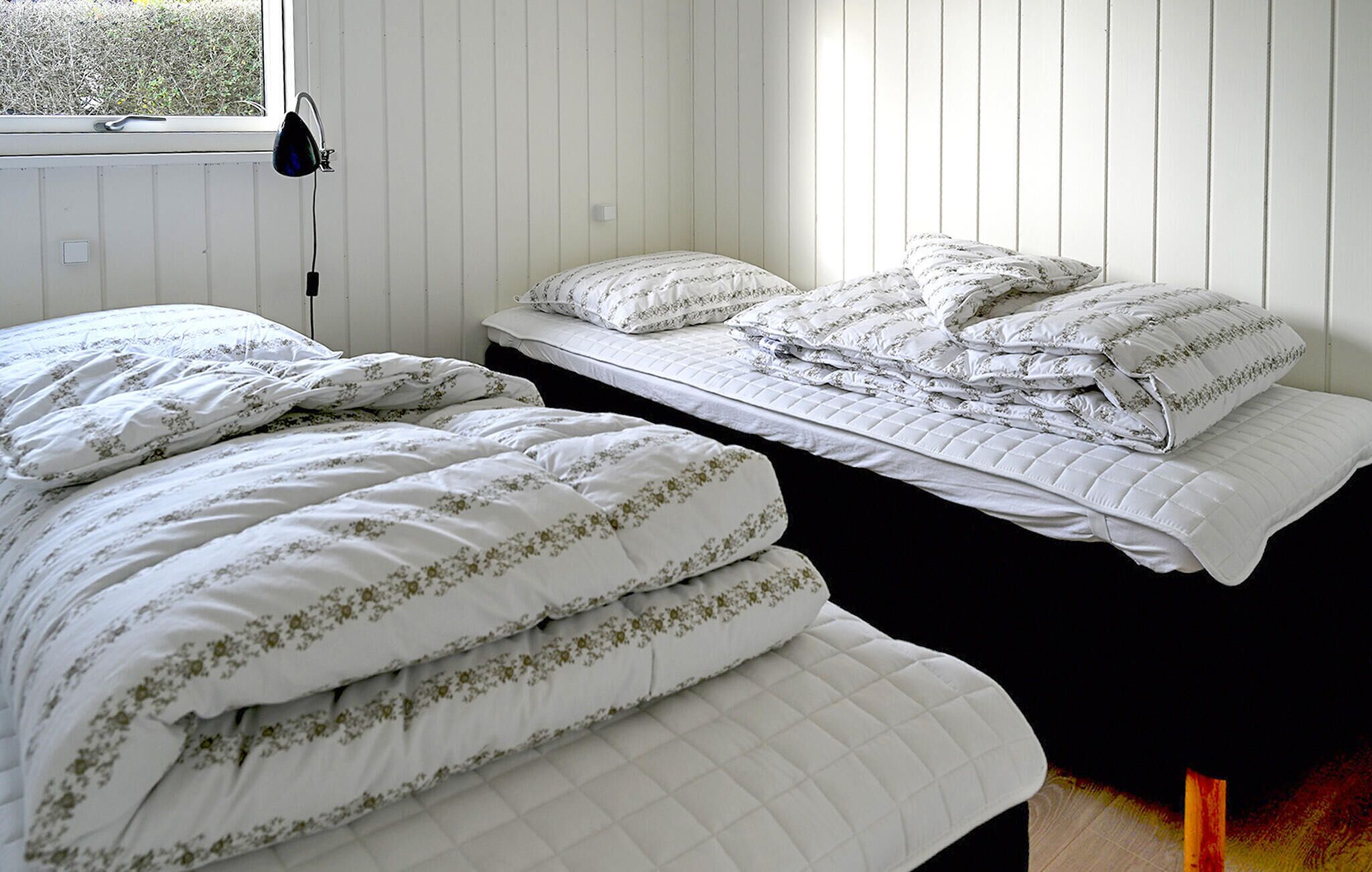Een slaapkamer met twee bedden, elk voorzien van witte beddengoed en bloemenmotieven. Een raam met gordijn en een lamp aan de linkerkant.