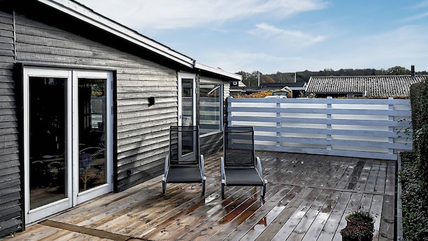 En træterrasse med to stole, en skydedør og et hvidt hegn.
