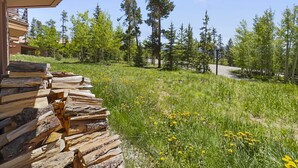 A wooden deck with logs, a clear sky, and a forested area with tall trees and yellow flowers. - Bb103 Buffalo Ge 2br 2ba 2 Bedroom Condo by RedAwning (Silverthorne)