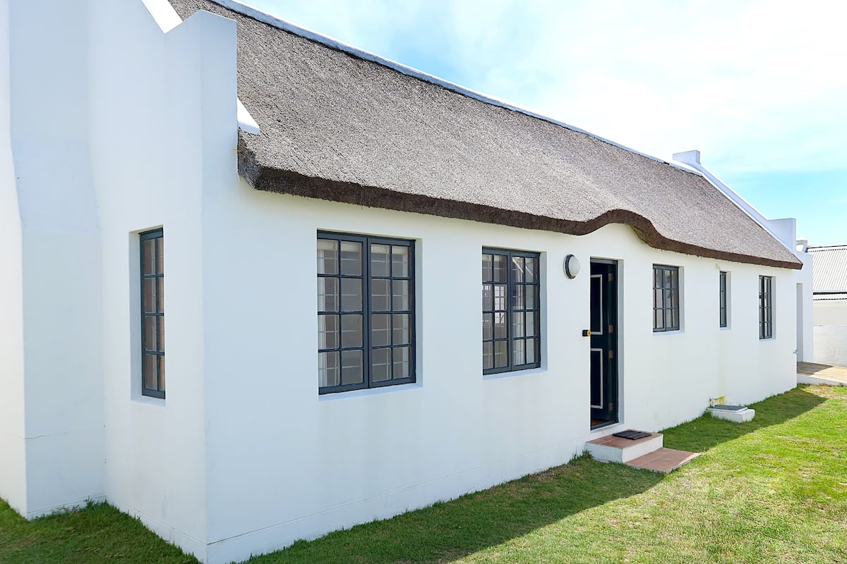 A single-story white building with a thatched roof, a front door, and three windows.