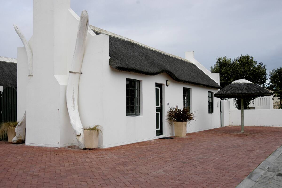 A white building with a thatched roof, potted plants, and a brick pathway.