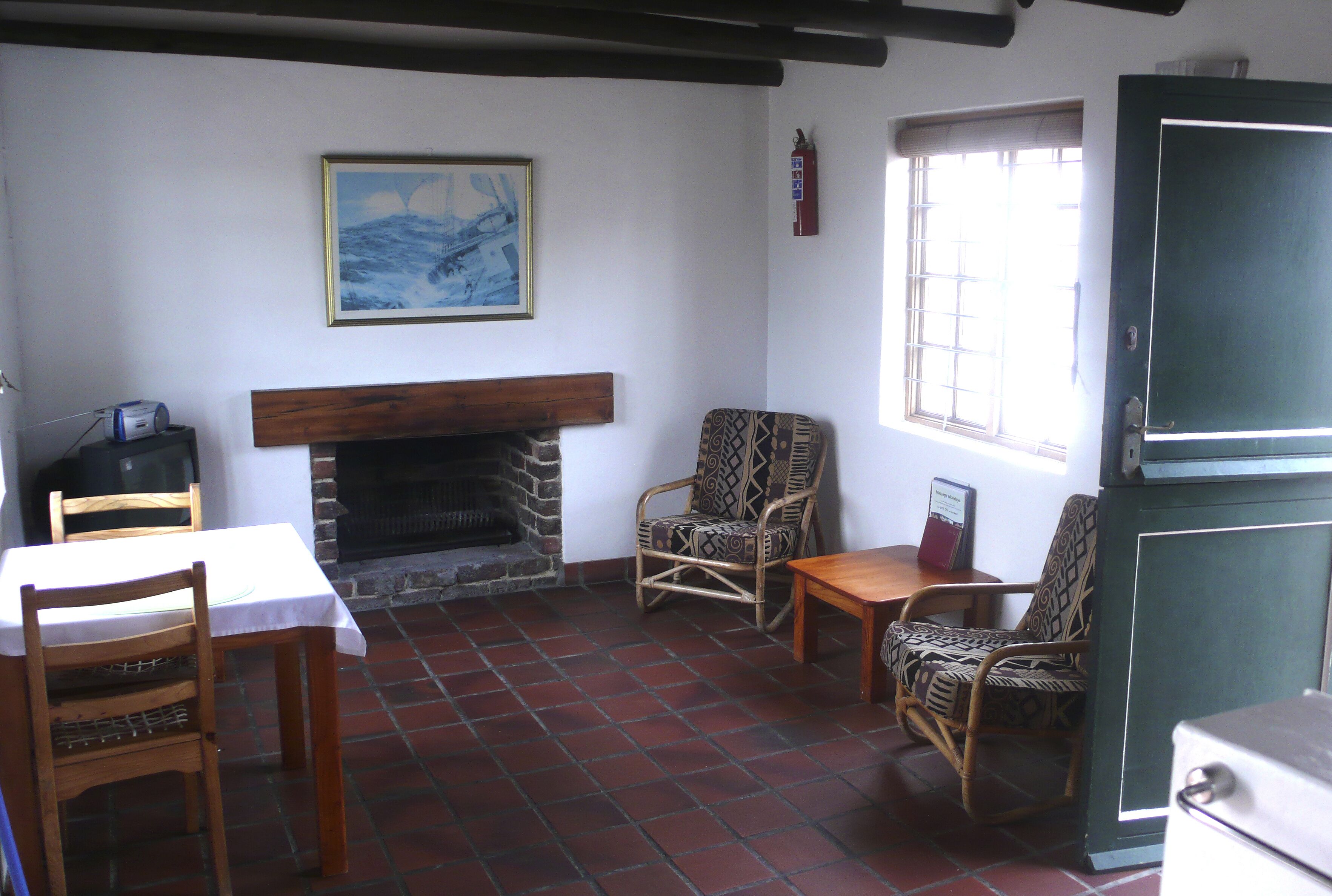 A room with a fireplace, patterned chairs, a table, and a window with blinds.