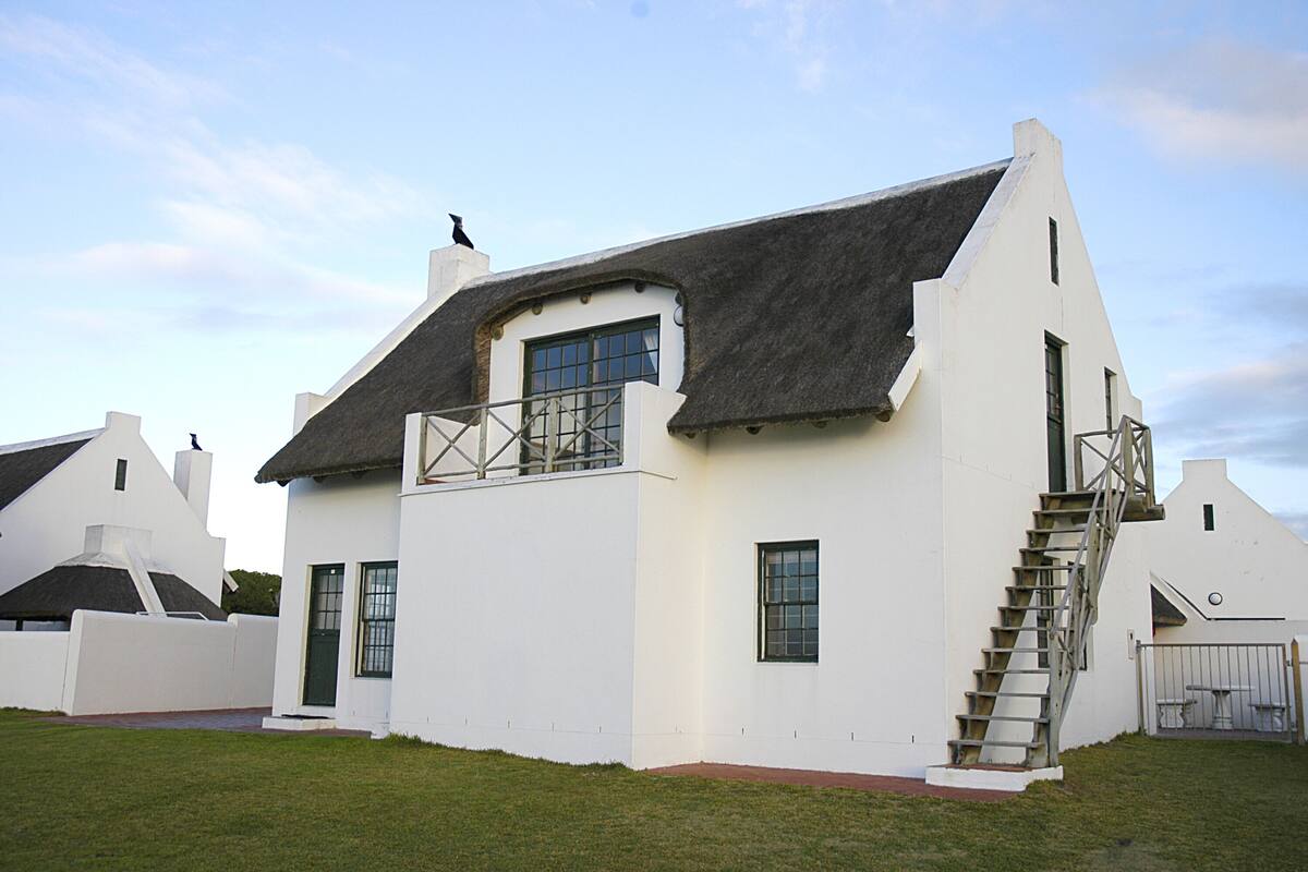 A white building with a thatched roof, a balcony, and a staircase leading to the entrance.