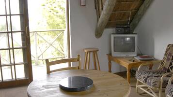 Una habitación acogedora con una mesa redonda de madera, dos sillas de madera, un televisor sobre una mesita y un sillón de mimbre.