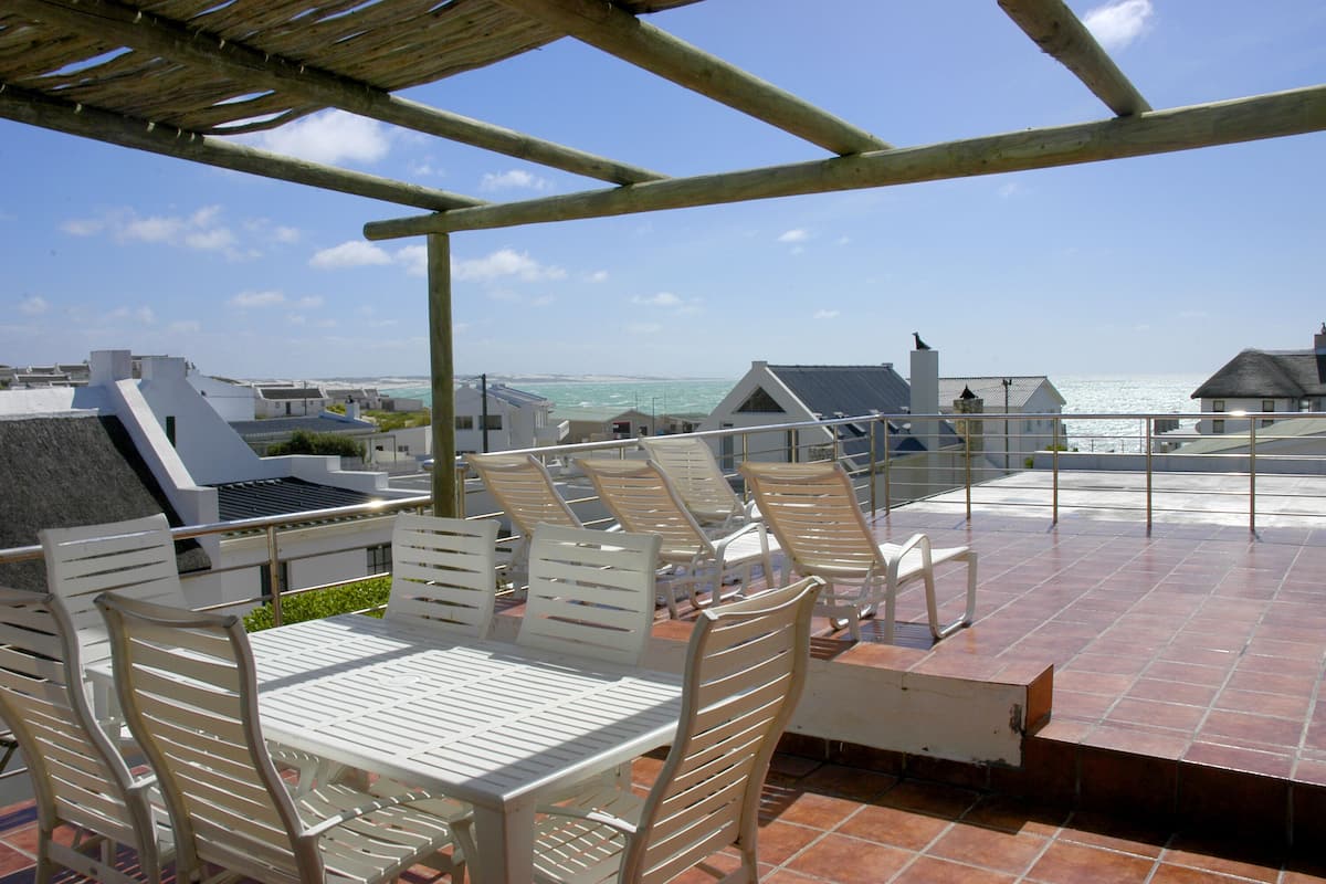 A terrace with white chairs and a table, overlooking the sea.