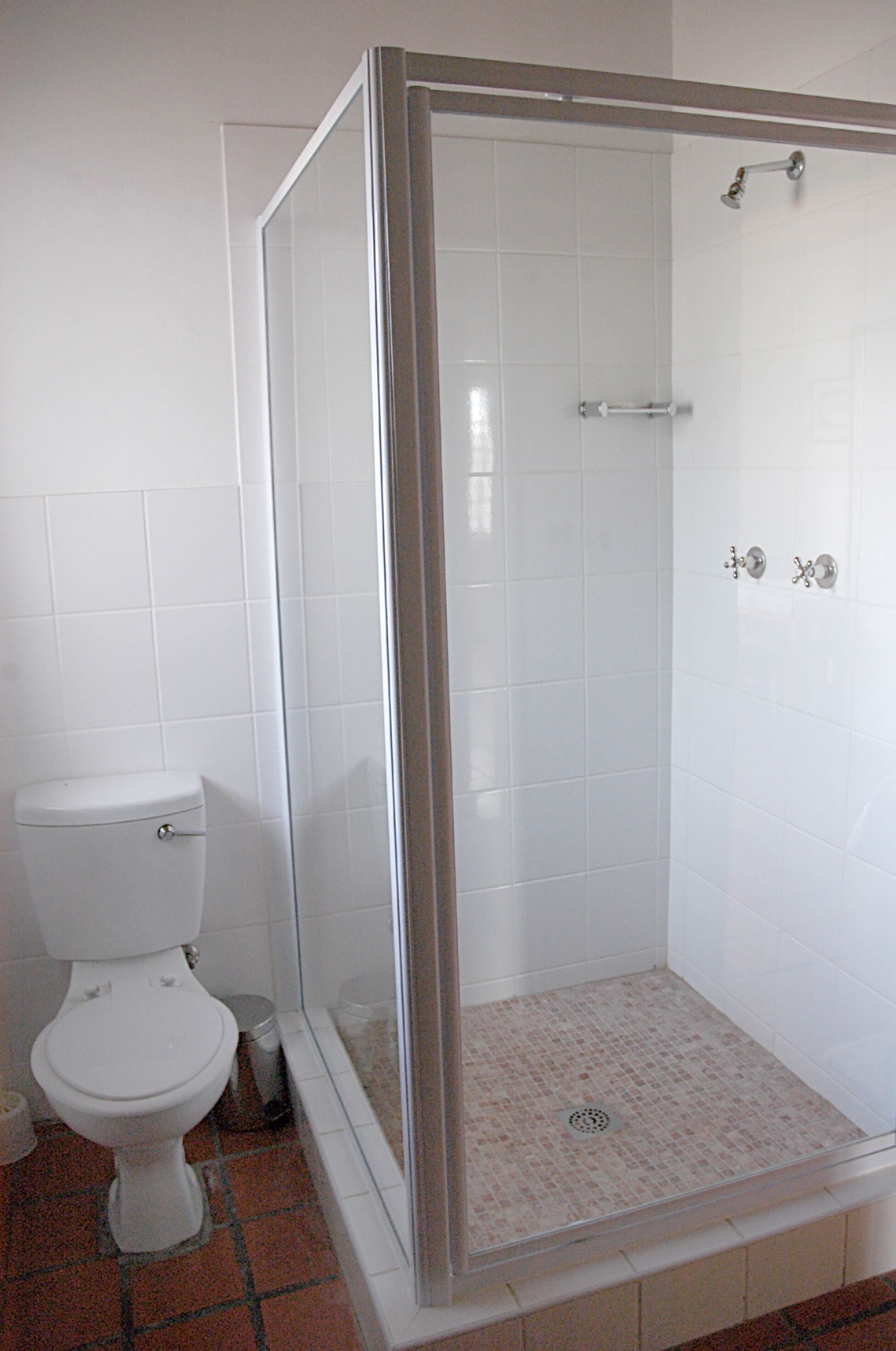 A bathroom with a toilet, a shower with a glass door, and tiled walls.