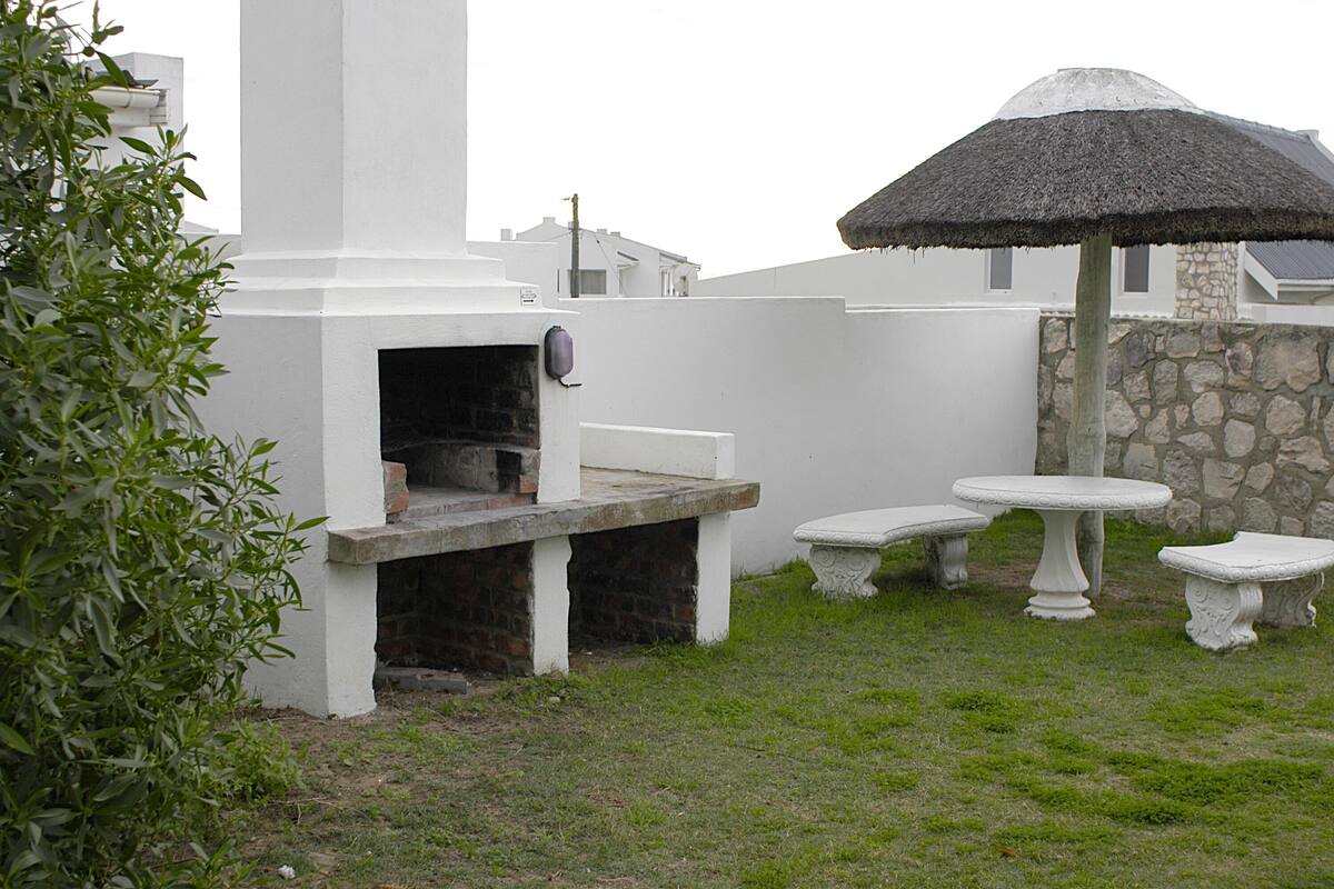 An outdoor kitchen area with a built-in oven, stone wall, and a thatched umbrella.