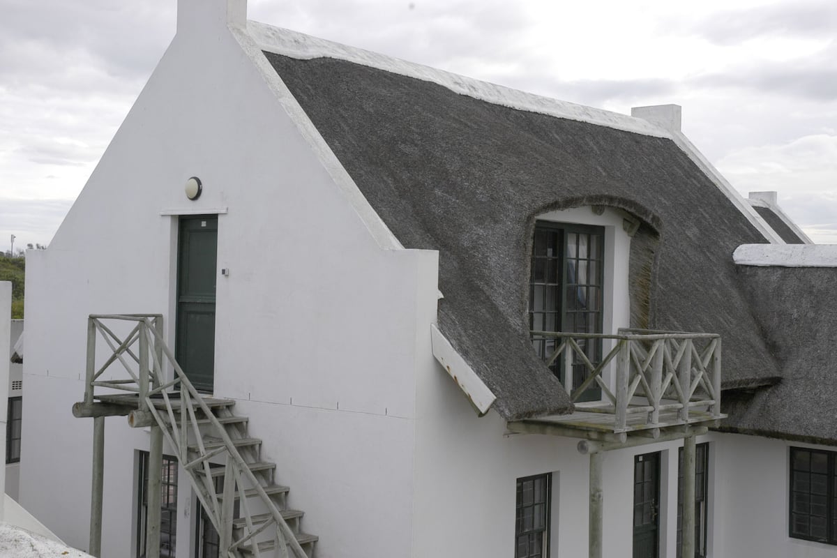 A white building with a steeply pitched roof, a small balcony, and a wooden staircase leading to a door.