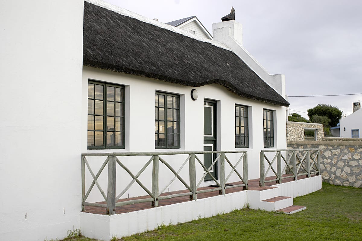 A white building with a black roof, multiple windows, and a stone wall.