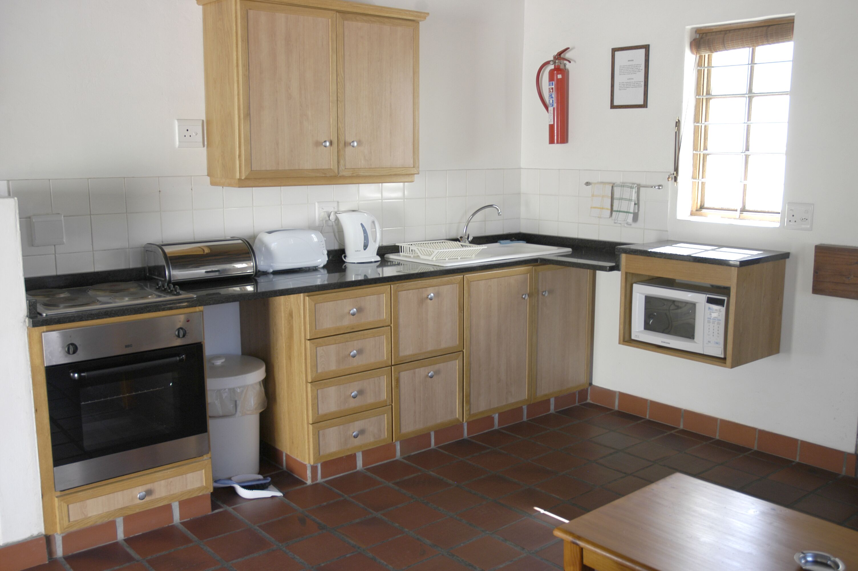 A kitchen with wooden cabinets, a built-in oven, a microwave, and a window with blinds.