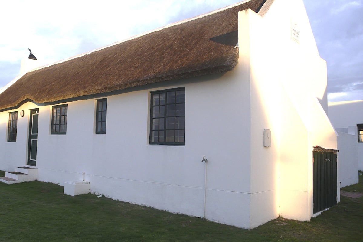 A white building with a thatched roof, multiple windows, and a small staircase leading to the entrance.