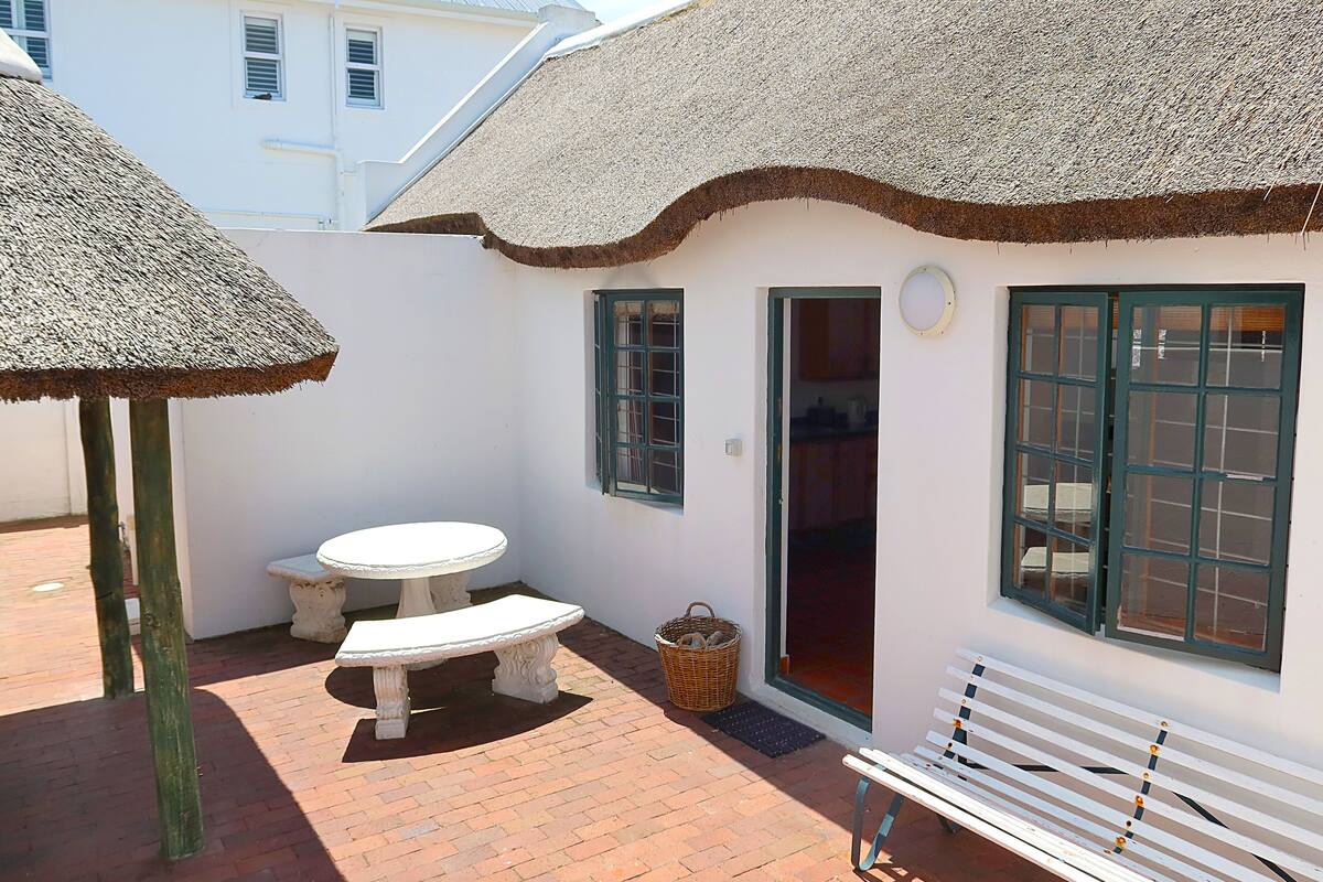 A small, white building with a thatched roof, a bench, a table, and a wicker basket.