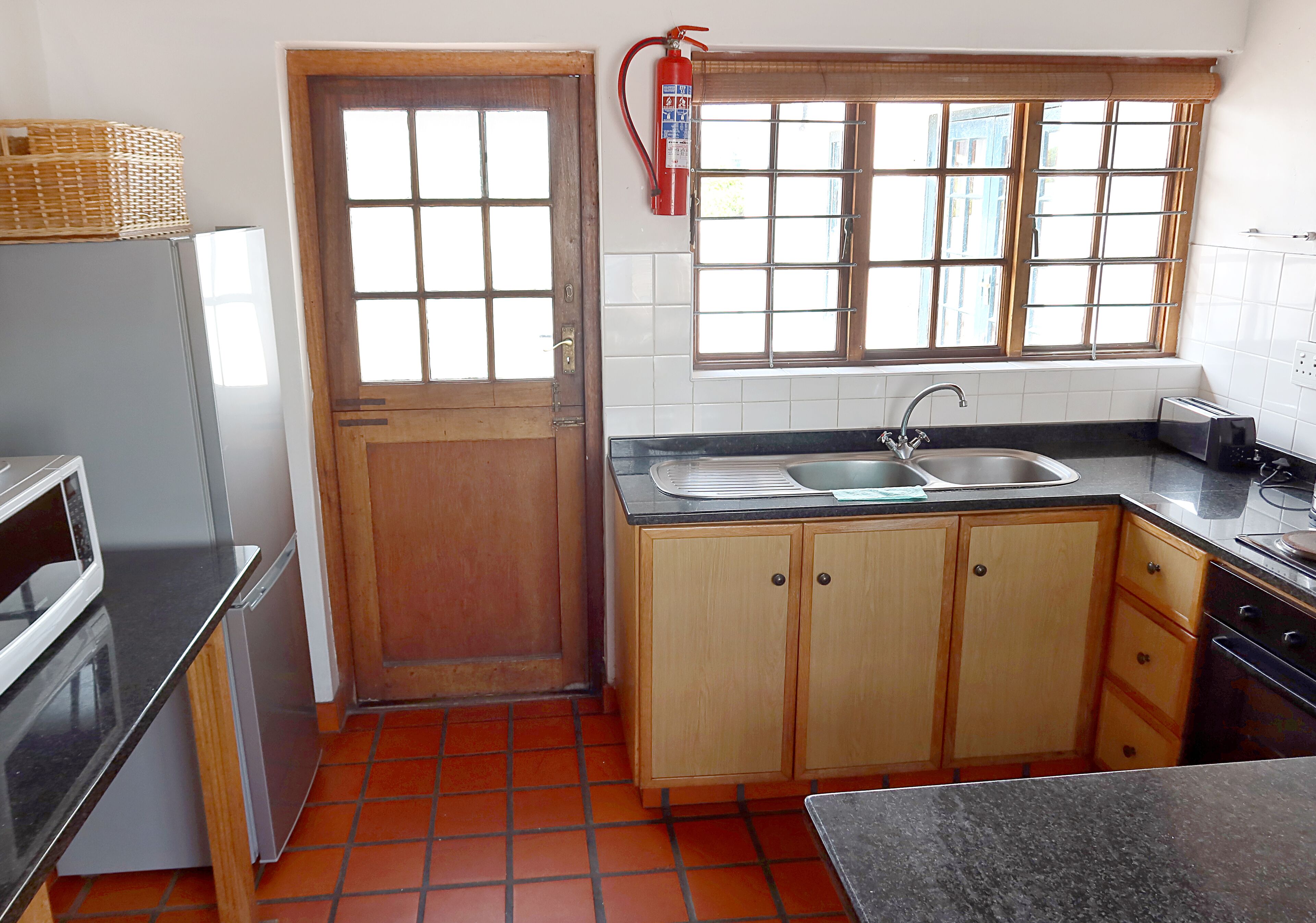 A compact kitchen with a refrigerator, a sink, wooden cabinets, and a window with blinds.