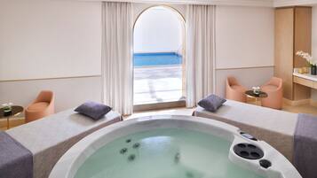 Relax in a serene spa room with a spacious hot tub, plush armchairs, and a pool view.