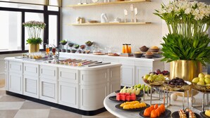 Une cuisine bien éclairée, dotée d’un îlot central, de meubles blancs et d’une variété de fruits et de boissons disposés en présentation.