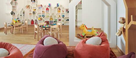 Une salle de jeux pour enfants avec un plancher en bois, une table avec des jouets et une bibliothèque contenant divers objets.