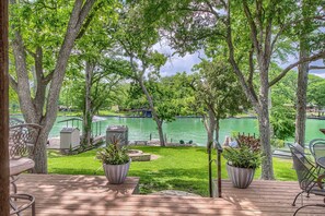 Terraza con mobiliario exterior, plantas en macetas y vista a un lago con barcos.