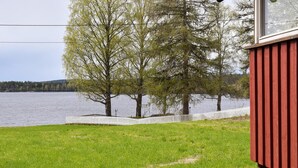 Een pand aan het meer, met een rode gevel, witte hek en bomen.