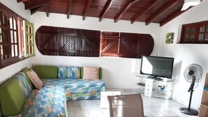 A cozy living room with a sofa, TV, fan, and a table with a decorative item. - Cosy nest - Plage de Babin (Morne-À-l'Eau Guadeloupe)