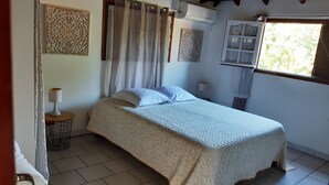 A bedroom with a bed, curtains, a window, and a wall-mounted air conditioner. - Cosy nest - Plage de Babin (Morne-À-l'Eau Guadeloupe)