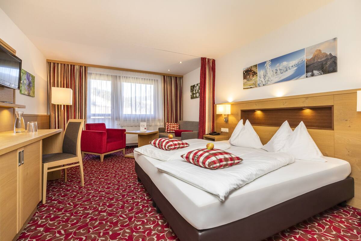 Una habitación de hotel con una cama grande, un escritorio con silla, un televisor y una ventana con cortinas.