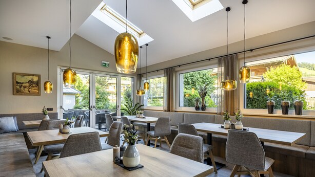 A modern restaurant with high ceilings, large windows, and natural light. Tables and seating are arranged for dining. - Hotel Pongauerhof (Flachau)