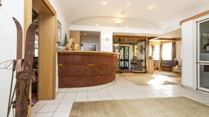 A spacious lobby with a curved reception desk, a large wooden door, and a seating area with a table and chairs. - Hotel Pongauerhof (Flachau)