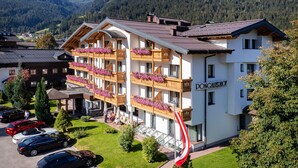 A multi-story hotel with balconies adorned with flowers, a flag, and a view of the surrounding mountains. - Hotel Pongauerhof (Flachau)