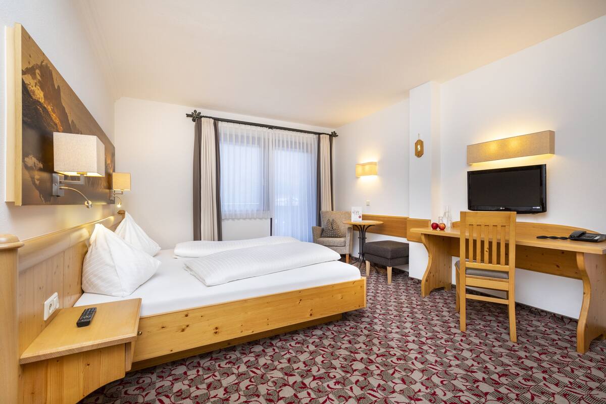 Habitación de hotel con cama, escritorio, silla, televisor y una mesita de noche con lámpara.