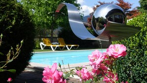 A swimming pool with lounge chairs and a reflective sculpture. - Hotel Pongauerhof (Flachau)