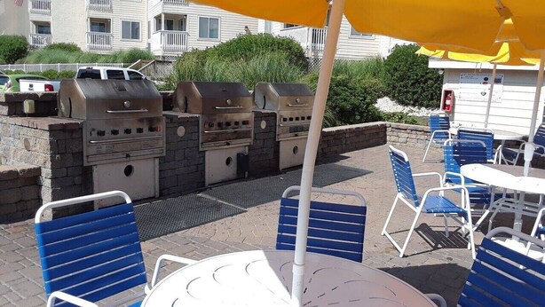 An outdoor patio with barbecue grills, blue chairs, and a yellow umbrella. - Wide, Sandy Beaches Await You! (Atlantic Beach)