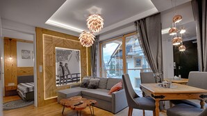 A modern living room with a wooden floor, a grey sofa, a wooden dining table with chairs, and pendant lights. - Apartament with Hot Tub (Zakopane)
