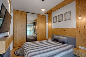 A modern bedroom with a wooden headboard, a bed with striped bedding, a round rug, and a large mirror. - Apartament with Hot Tub (Zakopane)