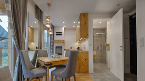 A modern kitchen with a wooden dining table, grey upholstered chairs, and pendant lighting. - Apartament with Hot Tub (Zakopane)